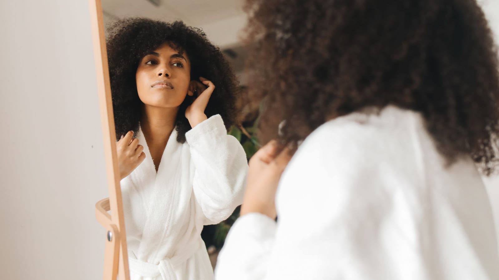 Woman with voluminous dark curls checking her curl definition in a mirror