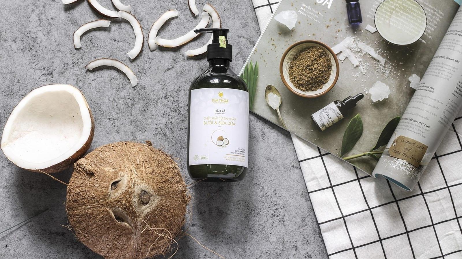 Bottle of natural hair oil with coconut halves on a bright table
