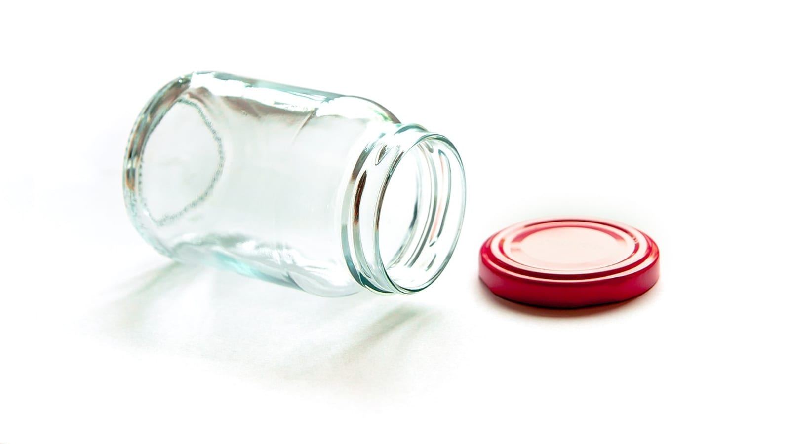Empty clear glass jar with a red lid lying on a white background