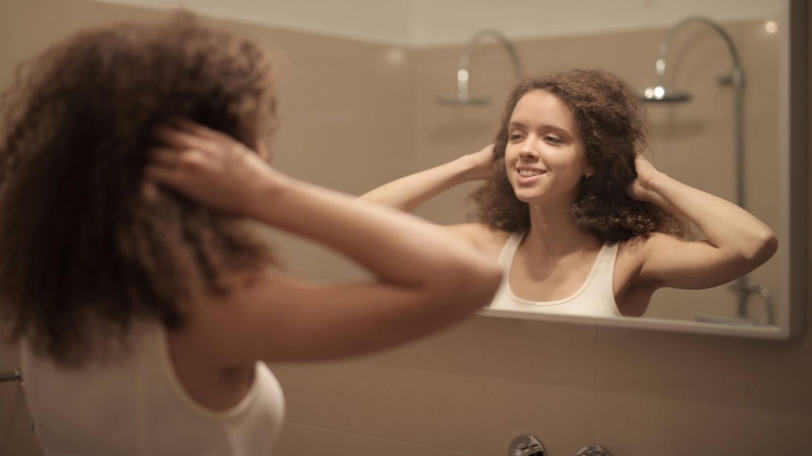 Woman fluffing her day-two curls in front of a bathroom mirror