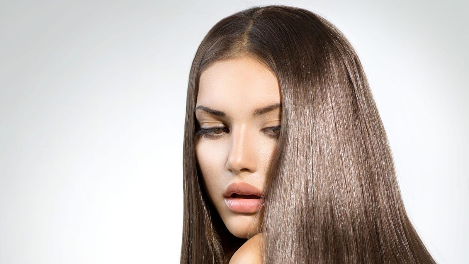 Woman with long, smooth, straight brunette hair against a gray background
