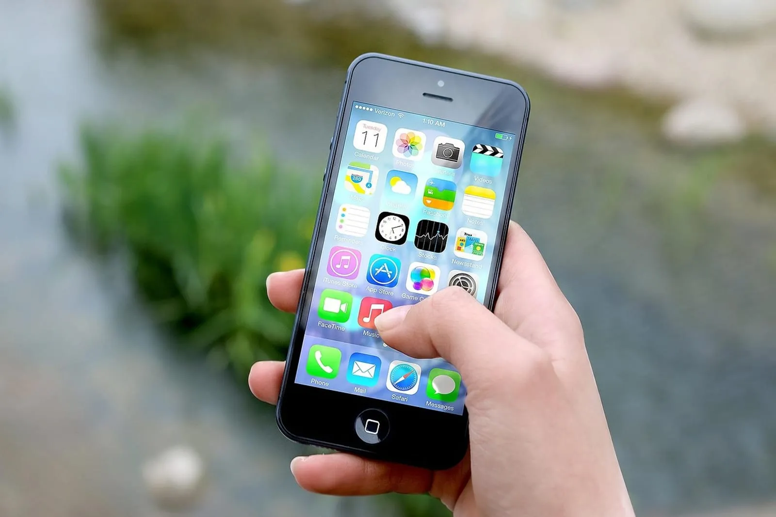 Hand holding an iPhone with a Home Screen full of app icons