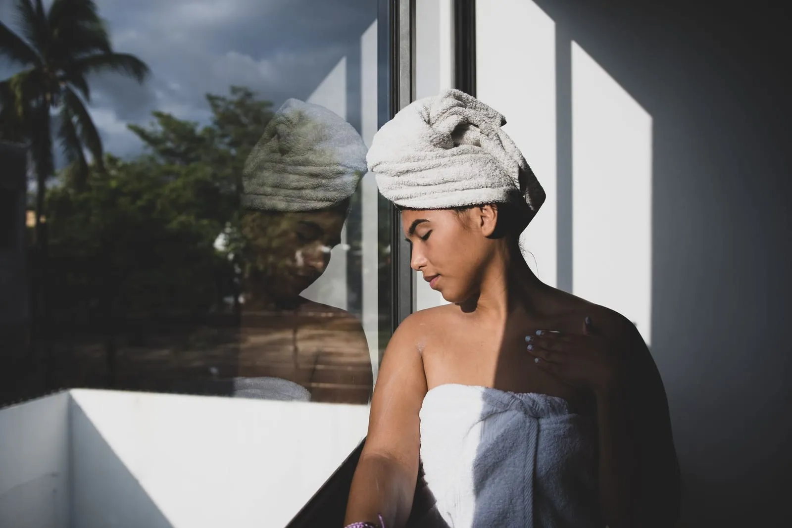 Woman with wet hair wrapped in a towel standing by a window