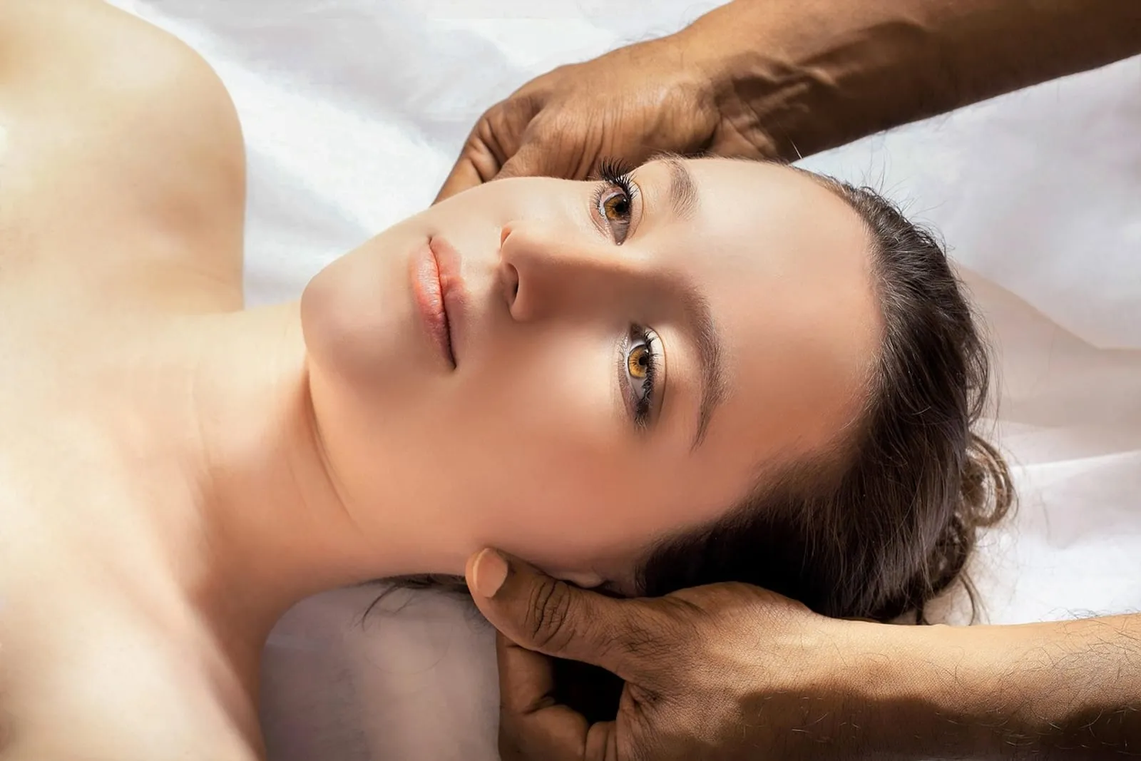 Woman lying down while a therapist massages her head and temples