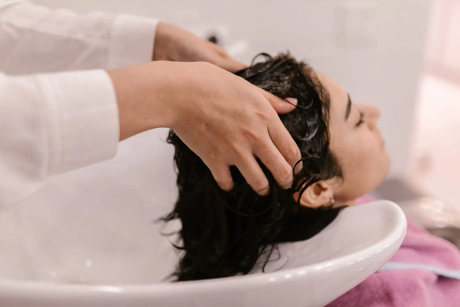 Fingertips massaging conditioner into the scalp of wet dark hair at a sink