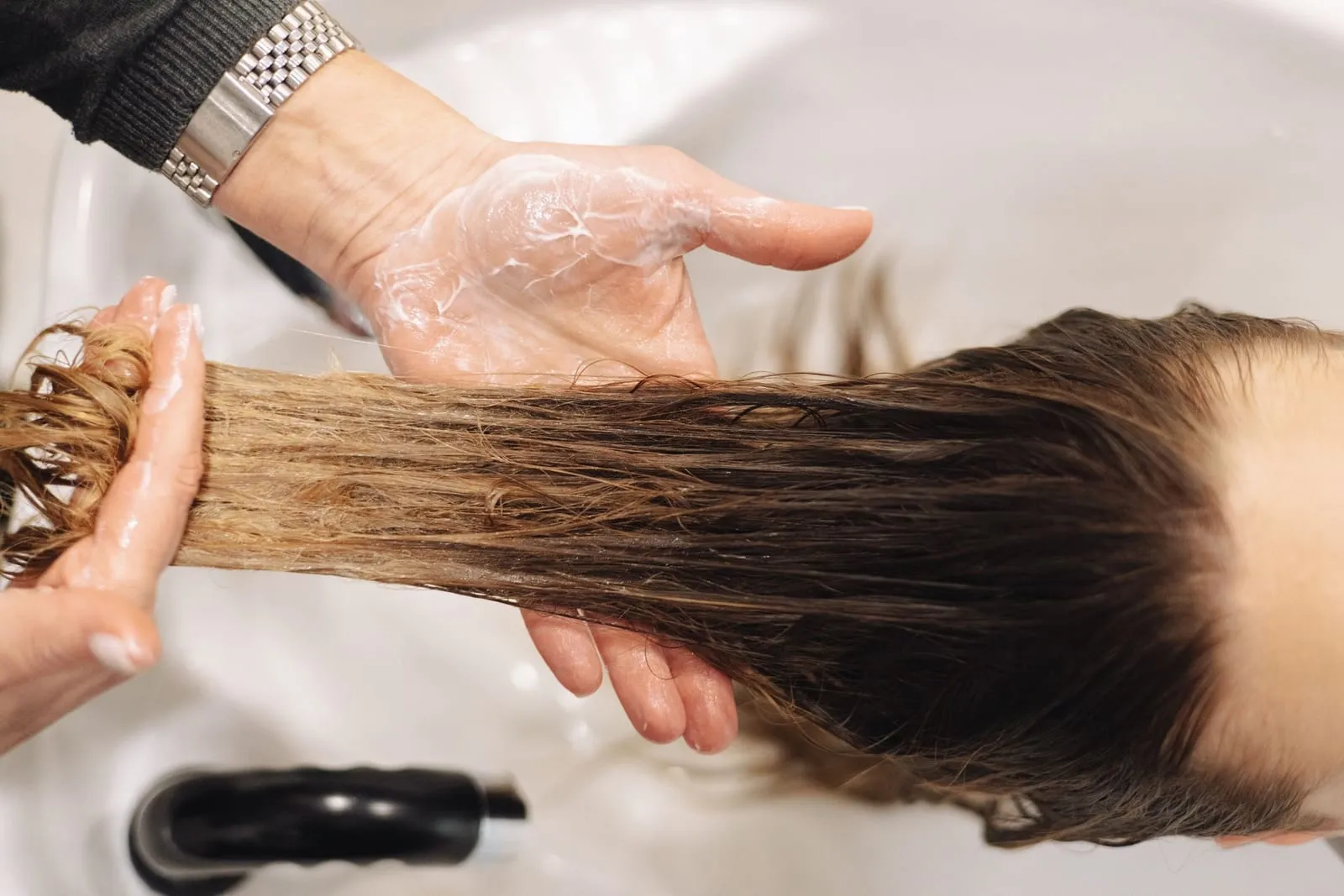 Hands working conditioner through long wet hair at a sink