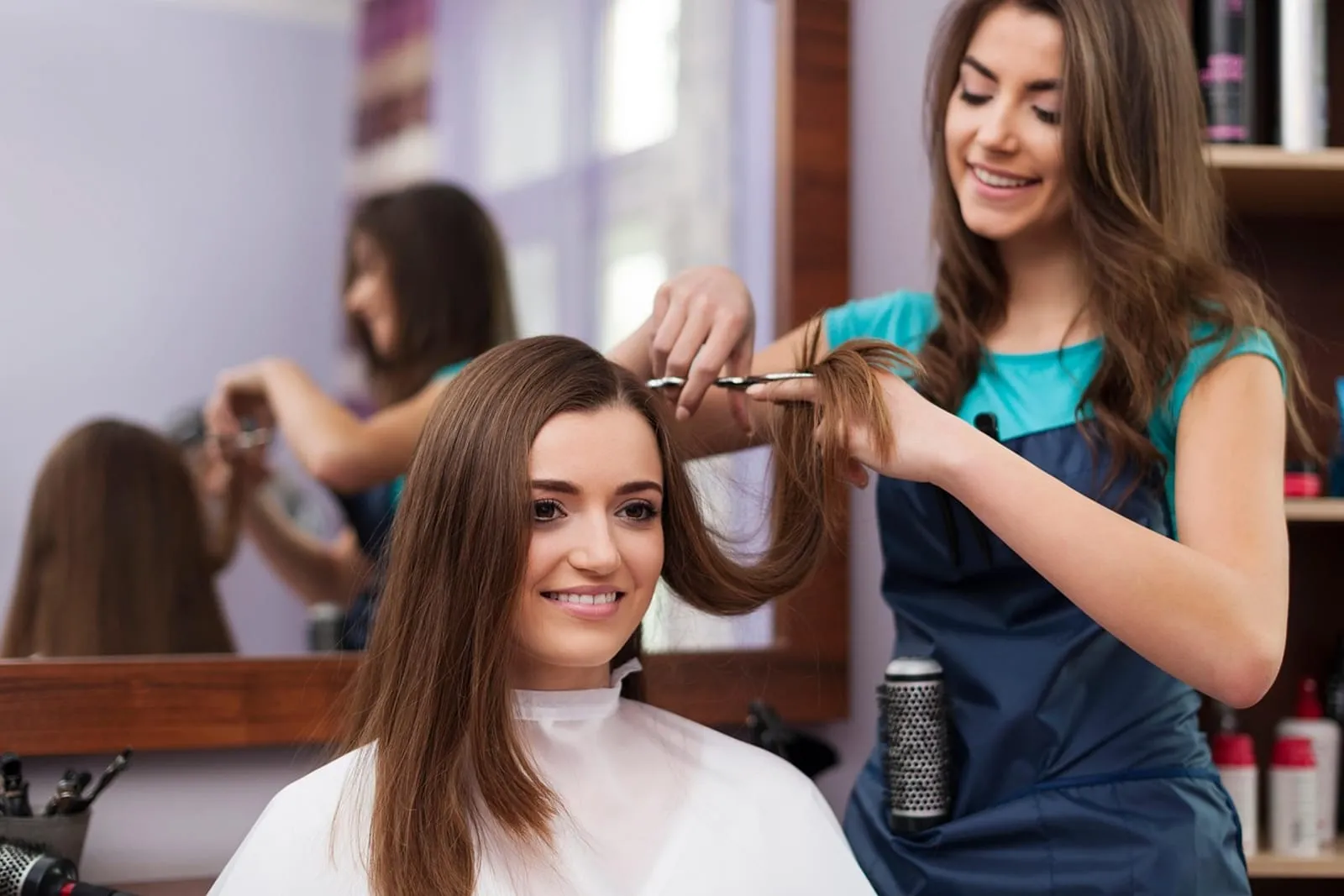 Stylist smoothing a section of a smiling client's hair in a salon