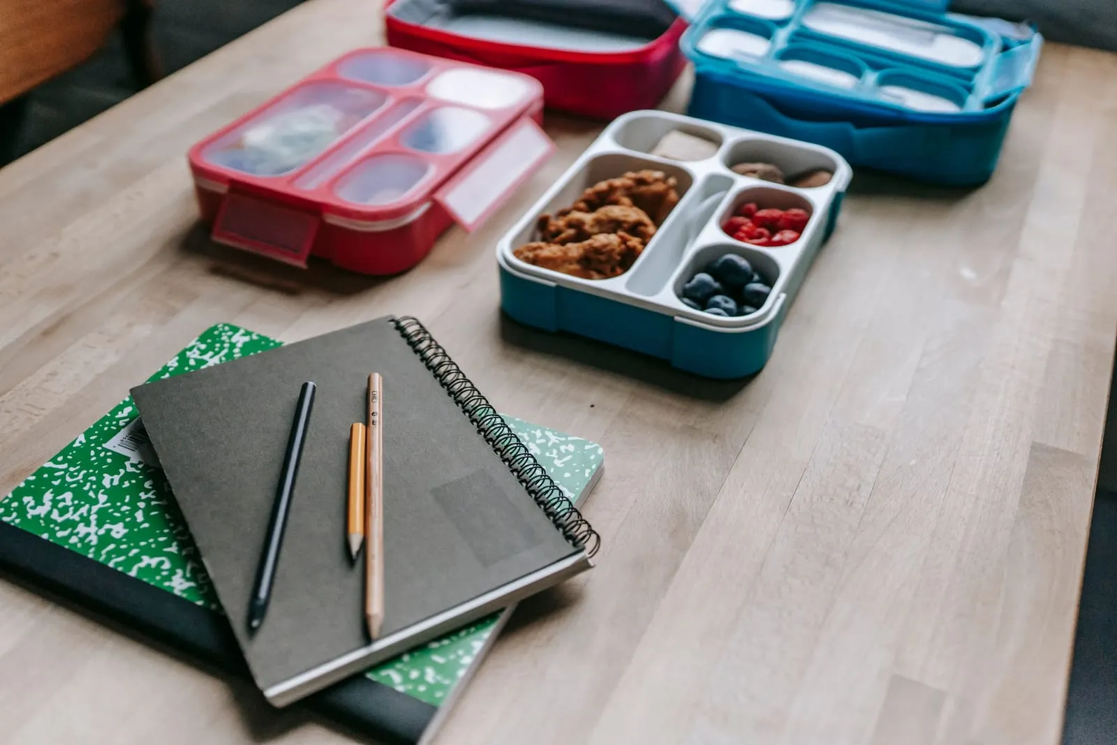 Packed lunch boxes with snacks next to a notebook and pencils on a table