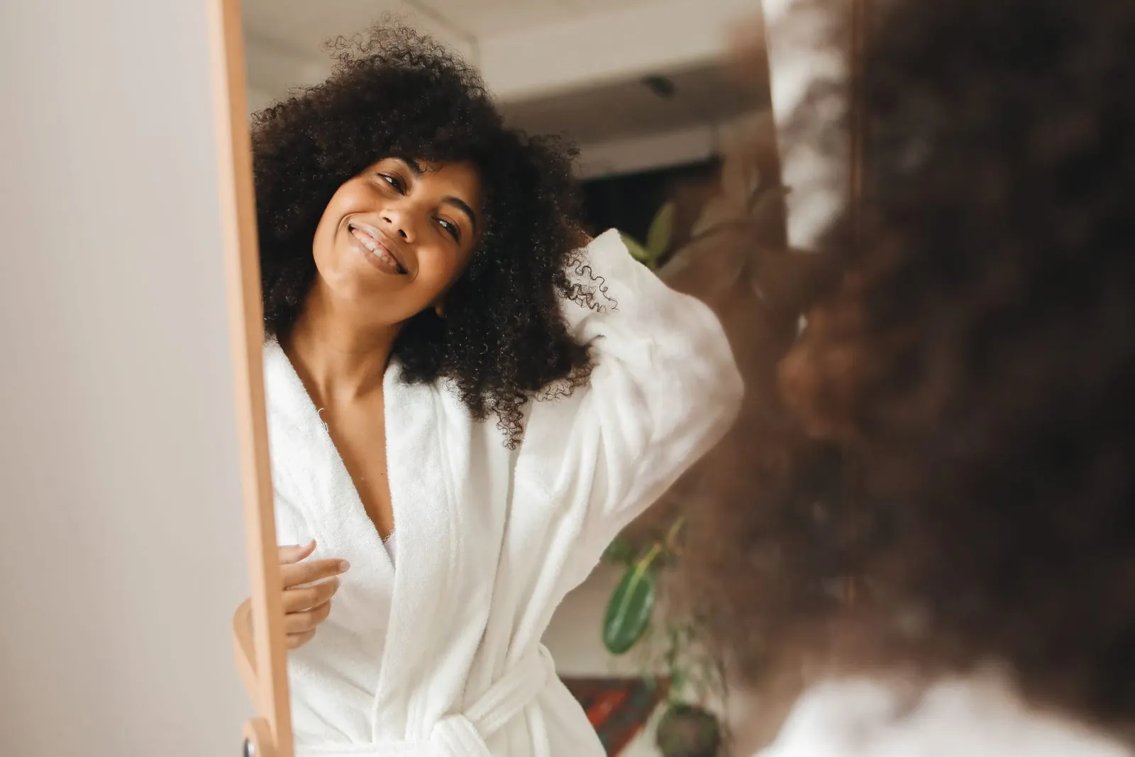 Smiling woman with refreshed, voluminous curls looking in a mirror