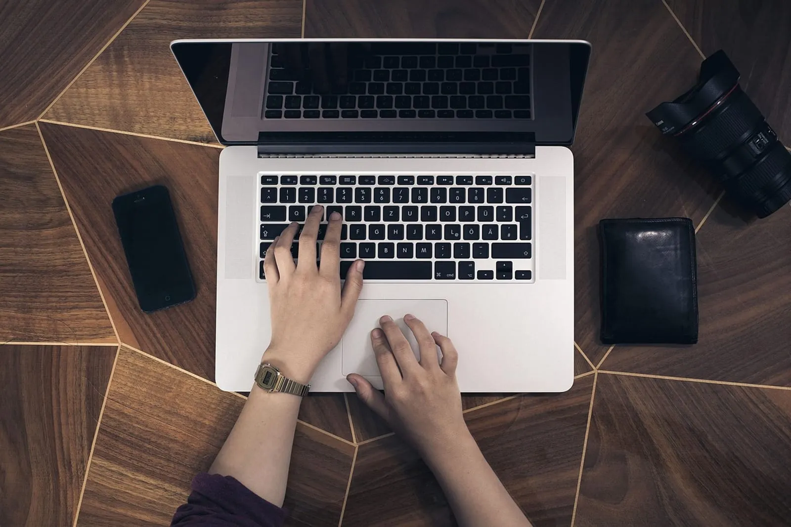 Overhead view of hands typing on a laptop next to a smartphone on a wooden desk