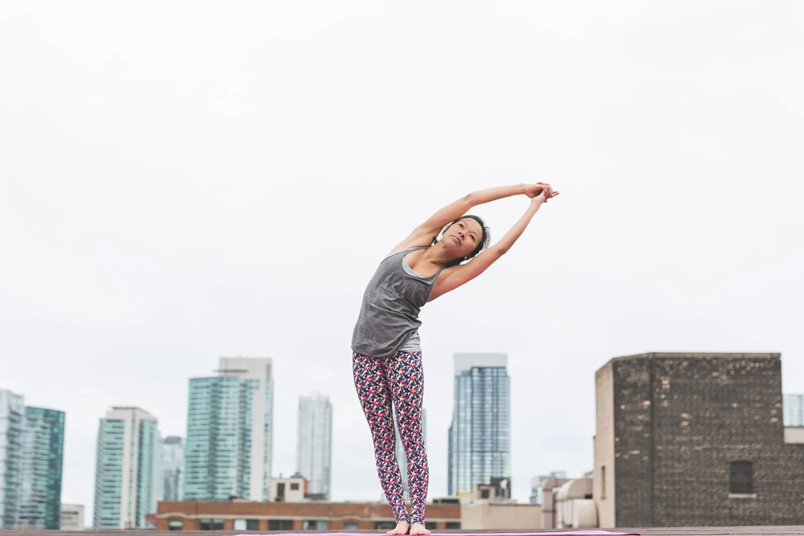 Woman stretching her arms overhead outdoors with a city skyline behind her