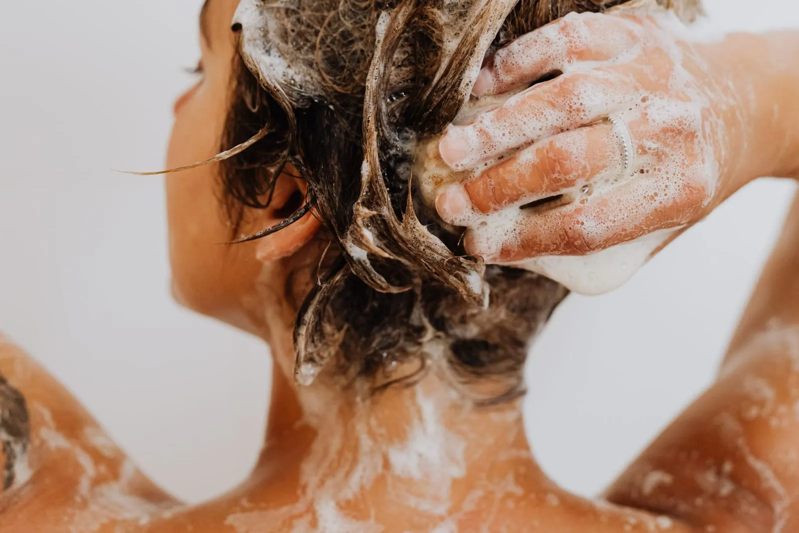 Woman massaging shampoo into her scalp with her fingertips in the shower